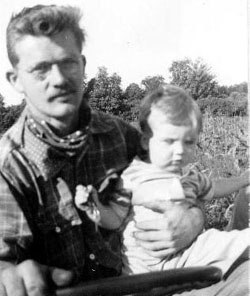 Melvin Sr. holding Melvin Jr. at wheel of tractor in front of cornfield