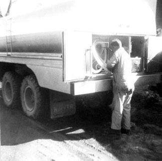 man in overalls handling tubes at rear of milk truck